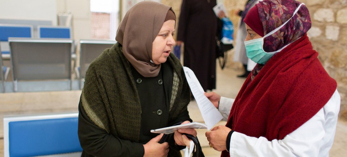 یک کارمند بهداشتی اطلاعات COVID-19 را به بیمار مراجعه کننده به مرکز بهداشت اورشلیم ارائه می دهد.